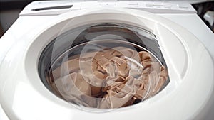 Clothes rotate counterclockwise in chrome drum from right to left. Washing machine is moving. Front view from bottom, an