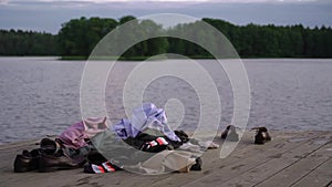 Clothes and shoes are on the pier. People undressed and swim naked in the lake.