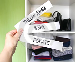 Clothes sorting in home wardrobe for donation, wearing and discard. Wear, Donate and Throw away paper notes in a hand on white