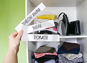 Clothes sorting in home wardrobe for donation, wearing and discard. Wear, Donate and Throw away paper notes in a hand on white