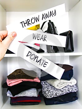 Clothes sorting in home wardrobe for donation, wearing and discard. Wear, Donate and Throw away paper notes in a hand on white