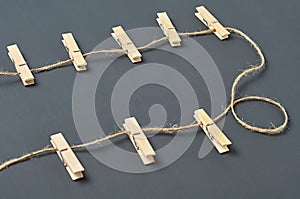 Clothesline with eight wooden clothespins and rope on background of dark concrete