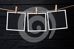 Clothespins with empty instant frames on twine against black wooden background. Space for text