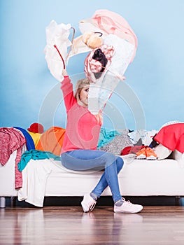 Woman sitting on messy couch throwing clothes
