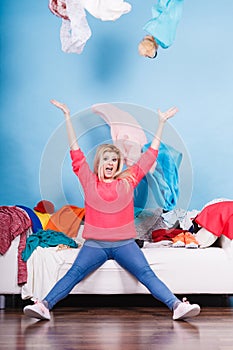 Woman sitting on messy couch throwing clothes