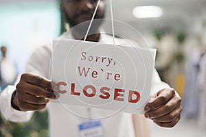 Clothing shop assistant holding sorry we are closed sign