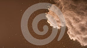 Cloud of fine, pale powder dispersing through the air against a brown backgroun photo