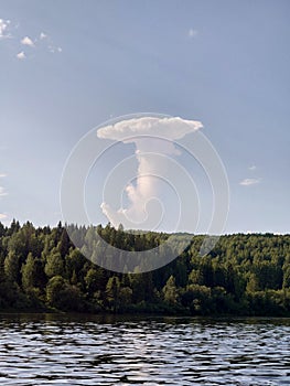 The cloud looks like a nuclear explosion. Clouds over the forest on the lake in summer