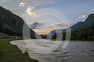 Cloud over the mountain range. Blue sky and green grass in the valley of a mountain river