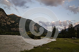 Cloud over the mountain range. Blue sky and green grass in the valley of a mountain river