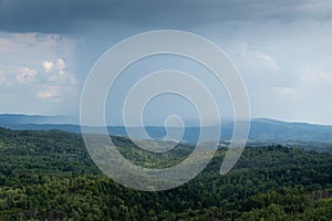 Cloudburst above hills overgrown in forests during summer