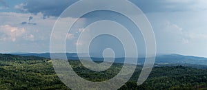 Cloudburst above hills overgrown in forests during summer