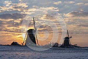 The clouds are beautifully colored during the sunrise on a cold winter morning with a snowy landscape at the three windmills in Le