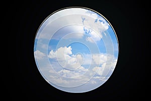 Clouds in blue sky outside round plane window