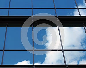 Clouds and bright blue sky reflected in the square mirrored windows of a modern commercial office building