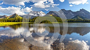 Clouds and Distant Rocky Mountain Peaks Background Reflected in Calm Blue Lake Water.