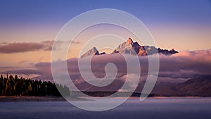 Clouds hanging over Jackson Lake as the sun rises and lights up the tallest peaks of Grand Teton National Park