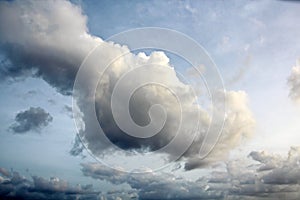 The clouds are multicolored, thunderous bizarre shapes against the blue sky and the sun above the ocean surface.