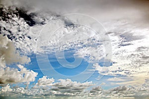 The clouds are multicolored, thunderous bizarre shapes against the blue sky and the sun above the ocean surface.