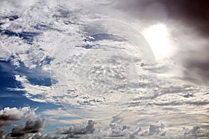 The clouds are multicolored, thunderous bizarre shapes against the blue sky and the sun above the ocean surface.