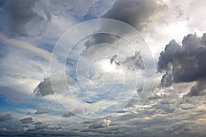 The clouds are multicolored, thunderous bizarre shapes against the blue sky and the sun above the ocean surface.