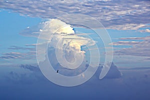 The clouds are multicolored, thunderous bizarre shapes against the blue sky and the sun above the ocean surface.