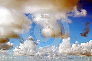 The clouds are multicolored, thunderous bizarre shapes against the blue sky and the sun above the ocean surface.