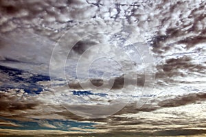 The clouds are multicolored, thunderous bizarre shapes against the blue sky and the sun above the ocean surface.