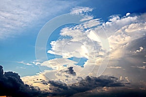 The clouds are multicolored, thunderous bizarre shapes against the blue sky and the sun above the ocean surface.