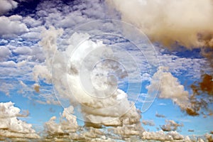 The clouds are multicolored, thunderous bizarre shapes against the blue sky and the sun above the ocean surface.