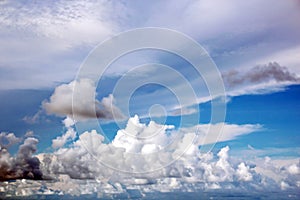 The clouds are multicolored, thunderous bizarre shapes against the blue sky and the sun above the ocean surface.