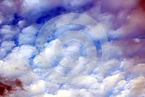 The clouds are multicolored, thunderous bizarre shapes against the blue sky and the sun above the ocean surface.