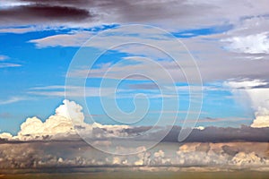 The clouds are multicolored, thunderous bizarre shapes against the blue sky and the sun above the ocean surface.