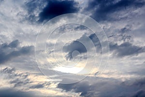 The clouds are multicolored, thunderous bizarre shapes against the blue sky and the sun above the ocean surface.