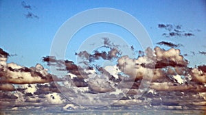 The clouds are multicolored, thunderous bizarre shapes against the blue sky and the sun above the ocean surface.