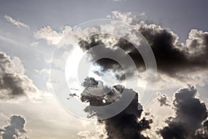 The clouds are multicolored, thunderous bizarre shapes against the blue sky and the sun above the ocean surface.