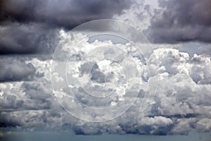 The clouds are multicolored, thunderous bizarre shapes against the blue sky and the sun above the ocean surface.