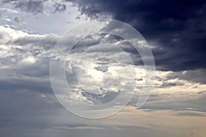 The clouds are multicolored, thunderous bizarre shapes against the blue sky and the sun above the ocean surface.