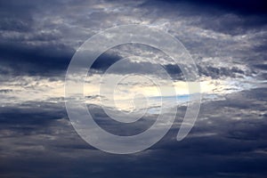 The clouds are multicolored, thunderous bizarre shapes against the blue sky and the sun above the ocean surface.