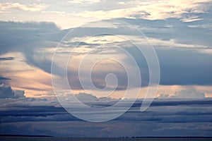 The clouds are multicolored, thunderous bizarre shapes against the blue sky and the sun above the ocean surface.