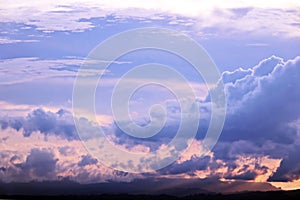 The clouds are multicolored, thunderous bizarre shapes against the blue sky and the sun above the ocean surface.