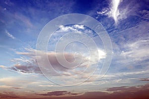 The clouds are multicolored, thunderous bizarre shapes against the blue sky and the sun above the ocean surface.