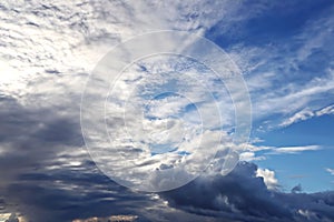 The clouds are multicolored, thunderous bizarre shapes against the blue sky and the sun above the ocean surface.