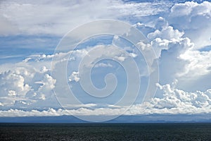 The clouds are multicolored, thunderous bizarre shapes against the blue sky and the sun above the ocean surface. Seascapes.