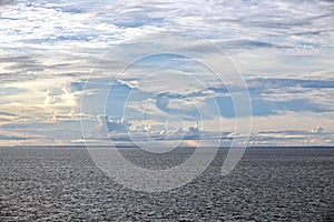 The clouds are multicolored, thunderous bizarre shapes against the blue sky and the sun above the ocean surface. Seascapes.