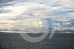 The clouds are multicolored, thunderous bizarre shapes against the blue sky and the sun above the ocean surface. Seascapes.