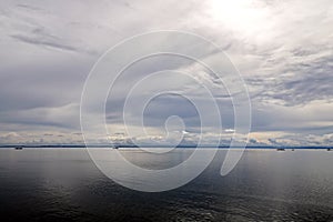 The clouds are multicolored, thunderous bizarre shapes against the blue sky and the sun above the ocean surface. Seascapes.