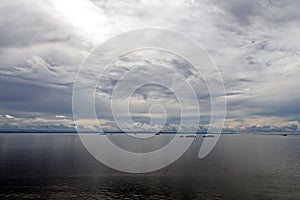 The clouds are multicolored, thunderous bizarre shapes against the blue sky and the sun above the ocean surface. Seascapes.