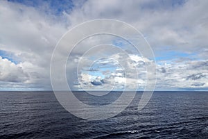 The clouds are multicolored, thunderous bizarre shapes against the blue sky and the sun above the ocean surface. Seascapes.