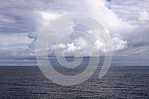 The clouds are multicolored, thunderous bizarre shapes against the blue sky and the sun above the ocean surface. Seascapes.